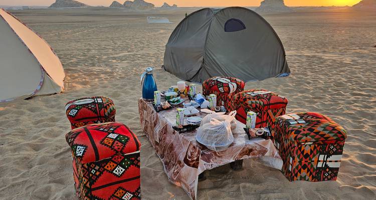 Desert campsite with set table and tents pitched on golden sand at sunrise.