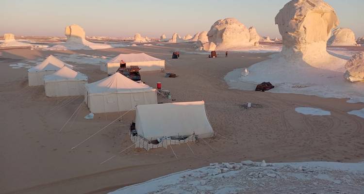 Cluster of canvas tents set among giant white desert monoliths in soft morning light.