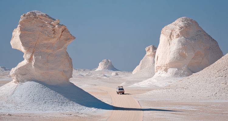 4x4 vehicle drives along a sandy track between towering chalk formations of the White Desert.