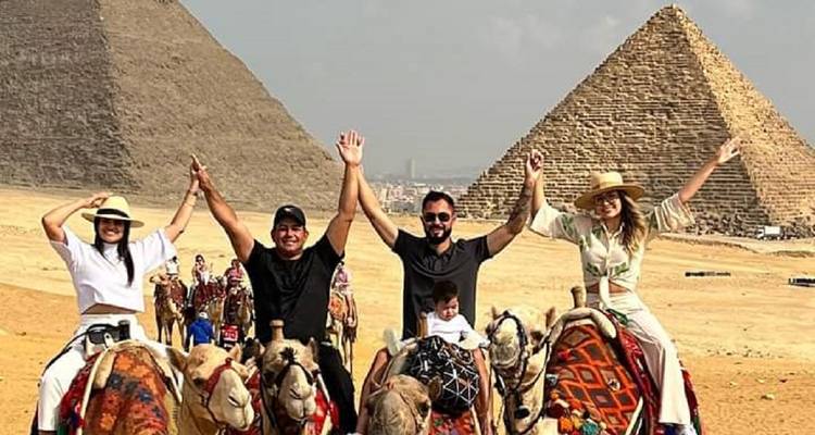Mensen op kamelen met piramides op de achtergrond.