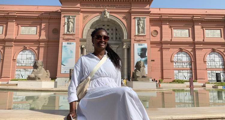 Stylish traveller in white dress posing outside the grand entrance of the Egyptian Museum in Cairo.