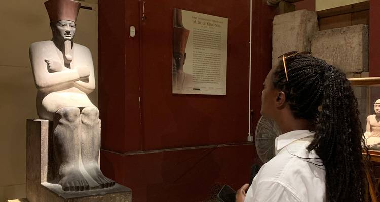Visitor closely observing a seated pharaoh statue inside the museum galleries.