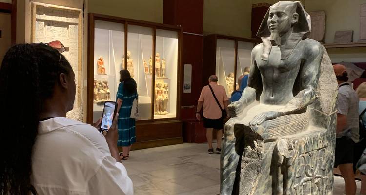 Tourist photographing an impressive pharaoh statue among other visitors in the museum hall.