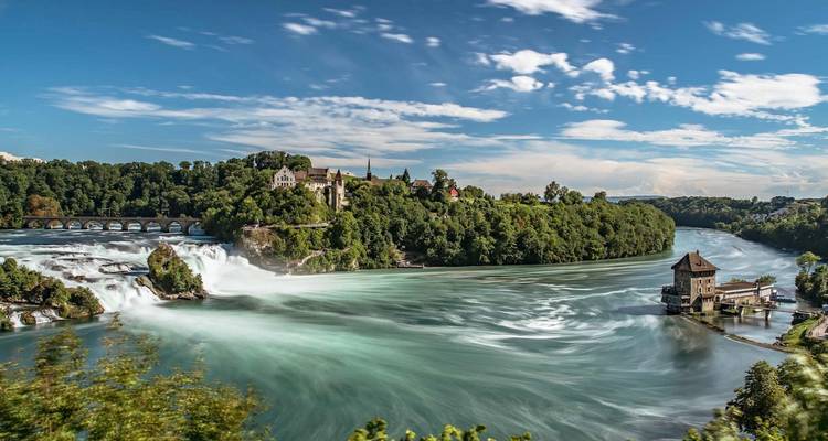 Chutes du Rhin avec une végétation luxuriante et un bâtiment historique au loin.
