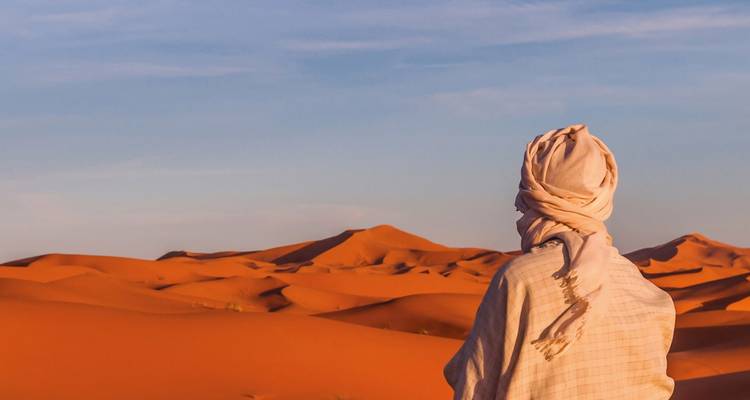 Voyageur solitaire en foulard traditionnel du désert contemplant de vastes dunes de sable orange au crépuscule