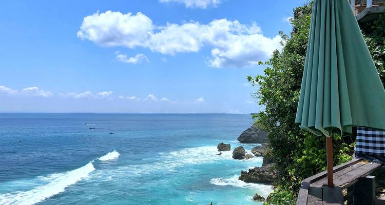 Klippenblick auf das Meer mit einem großen Sonnenschirm und üppigem Grün.