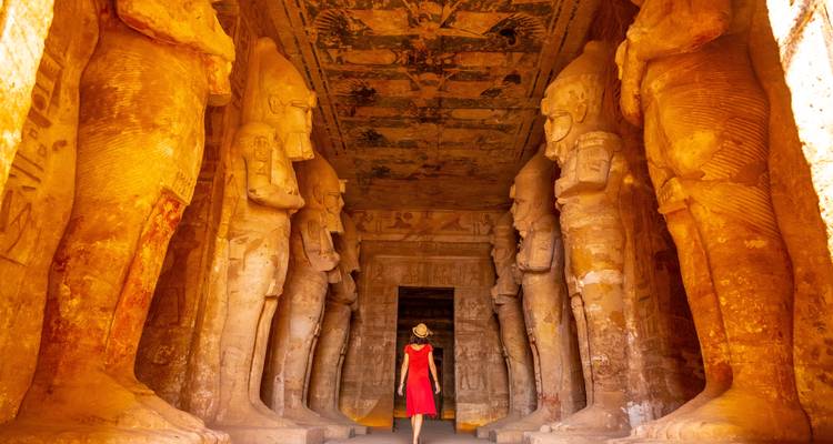 Een persoon die door een oude Egyptische tempel loopt met hoge standbeelden.