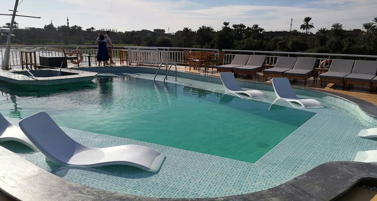 Pequeña cubierta de piscina en un crucero del Nilo con tumbonas modernas y un pasajero admirando el paisaje del río.