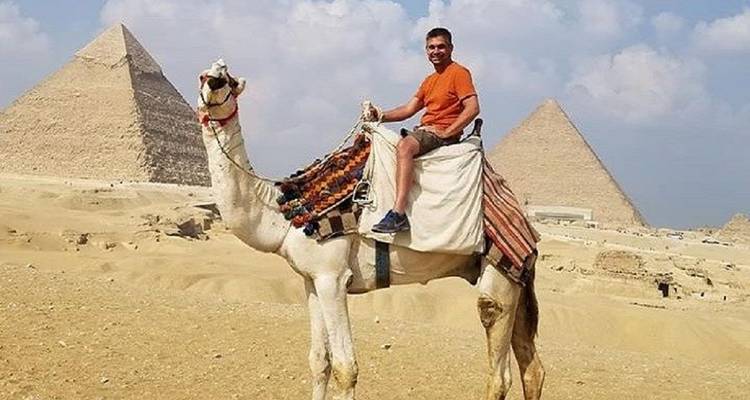 Visiteur à dos de chameau devant les pyramides sous un ciel bleu.