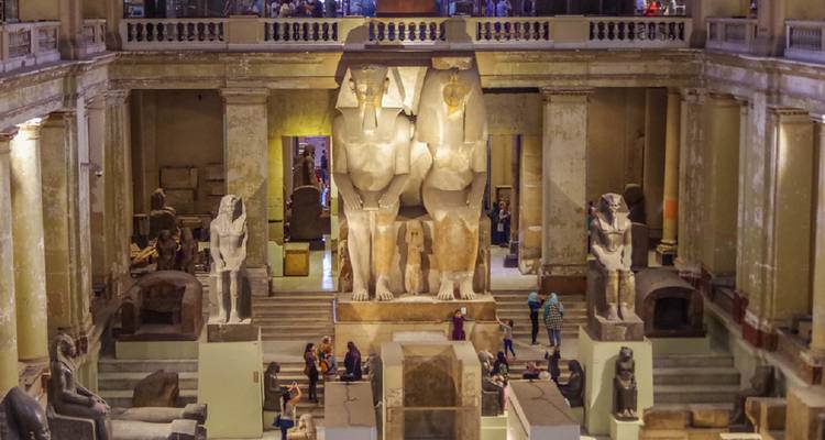 Grand hall à l'intérieur du Musée égyptien avec d'imposantes statues antiques et des visiteurs en contrebas.
