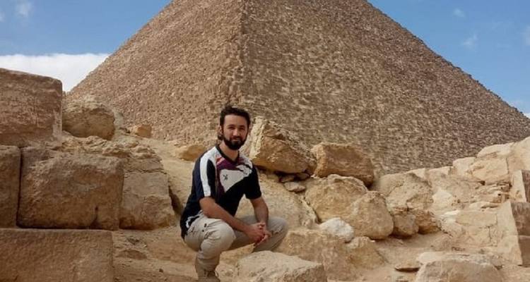 Voyageur accroupi sur des pierres près de la base d'une pyramide.