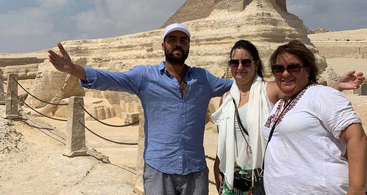 Trois voyageurs posent les bras étendus à côté du Sphinx par un après-midi ensoleillé dans le désert.