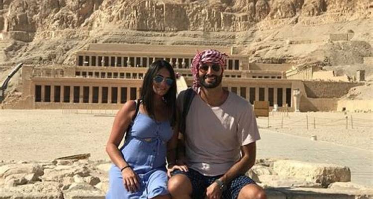Pareja sentada frente a un templo antiguo tallado en un acantilado.