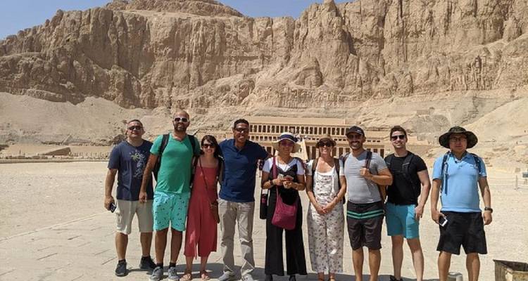 Grupo de turistas posando frente a un templo antiguo tallado en el acantilado.