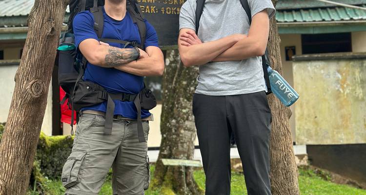 Deux personnes posant avec des sacs à dos, debout dans une zone boisée près d'un panneau.