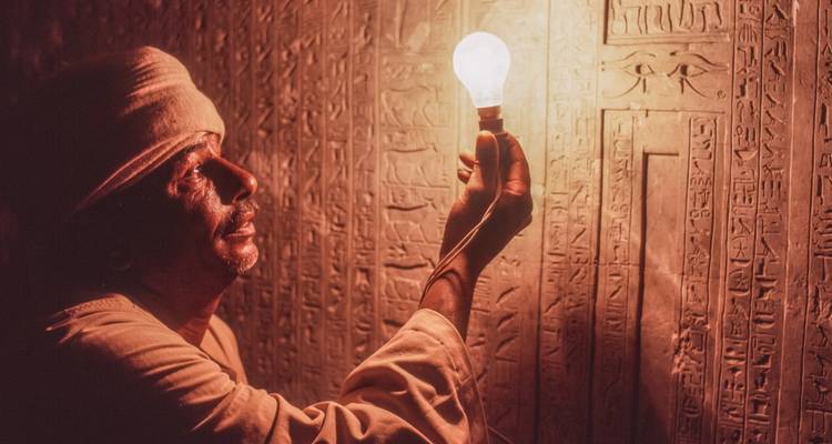 Een man die hiërogliefen op een muur observeert terwijl hij een gloeiende lamp vasthoudt.