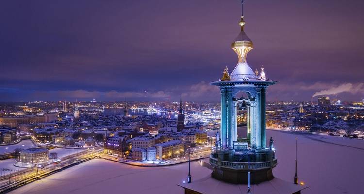 La torre iluminada del Ayuntamiento de Estocolmo se alza sobre los tejados nevados en un cielo crepuscular de color púrpura.