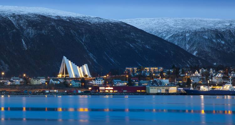 Abendliche Blaulichtstunde in Tromsø mit der Eismeerkathedrale und schneebedeckten Hügeln, die sich in ruhigem Wasser spiegeln