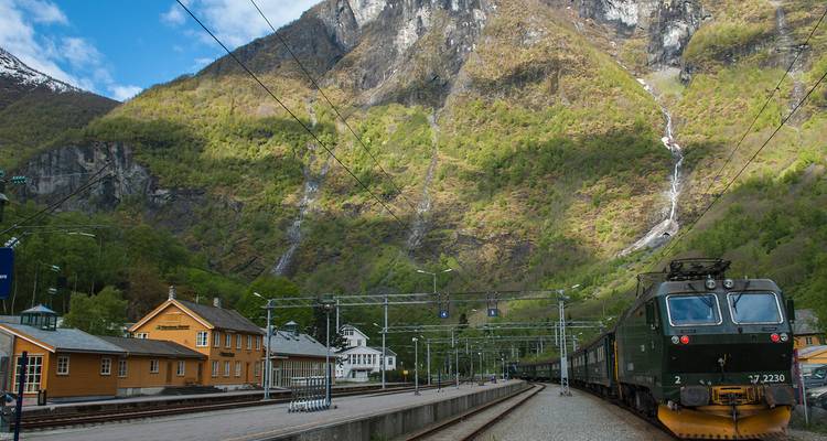Gare ferroviaire dans une région montagneuse avec cascade en arrière-plan.