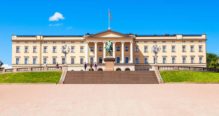 Palais Royal néoclassique à Oslo précédé d'un large escalier et d'une statue sous un ciel bleu éclatant.