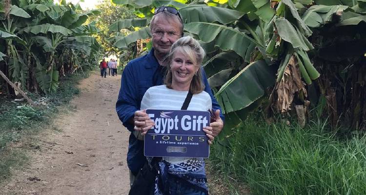 Lächelndes Paar hält ein 'Egypt Gift Tours' Schild auf einem blattreichen Plantagen-Pfad.