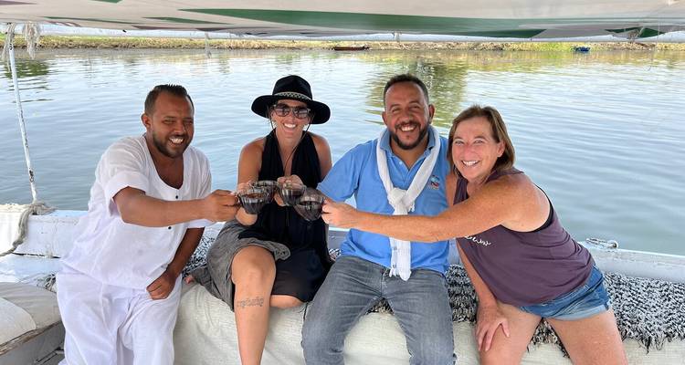 Vier Reisende stoßen gemeinsam mit Getränken auf einem ruhigen Flussboot an.