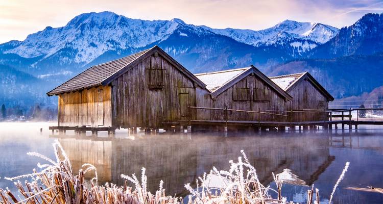 Matin brumeux au bord d'un lac avec des bateaux et des montagnes en arrière-plan.