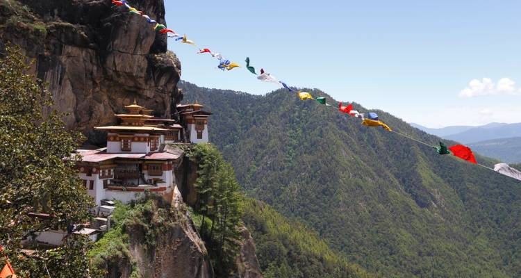 Un monastère sur une falaise, avec des drapeaux de prière colorés au premier plan.
