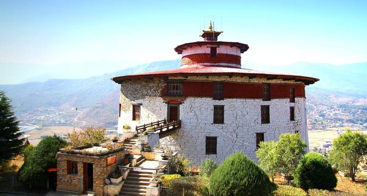 Un bâtiment traditionnel bhoutanais avec un toit circulaire entouré d'arbres.