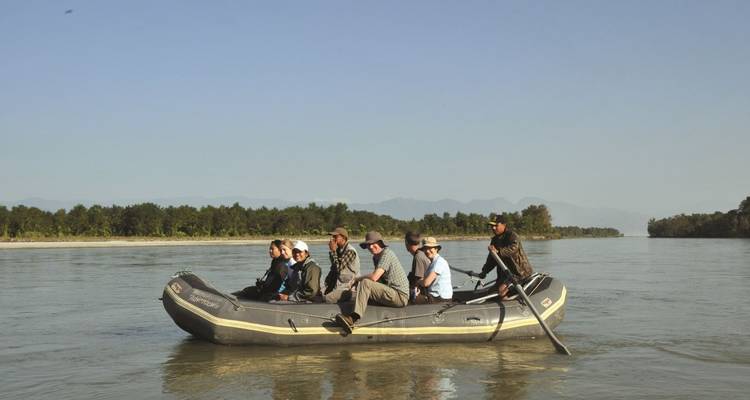 Eine Gruppe von Menschen in einem Floß auf einem Fluss mit Bäumen im Hintergrund.