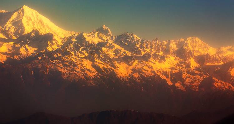 Des montagnes enneigées sous une lumière dorée, créant un horizon dramatique.