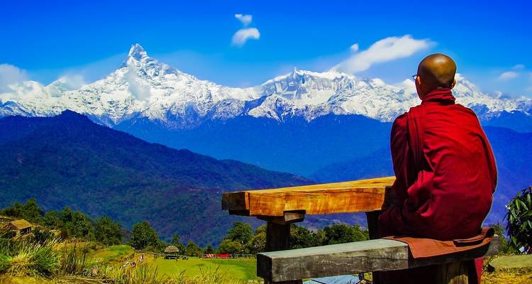 Person in traditional attire meditating in front of snowy peaks.