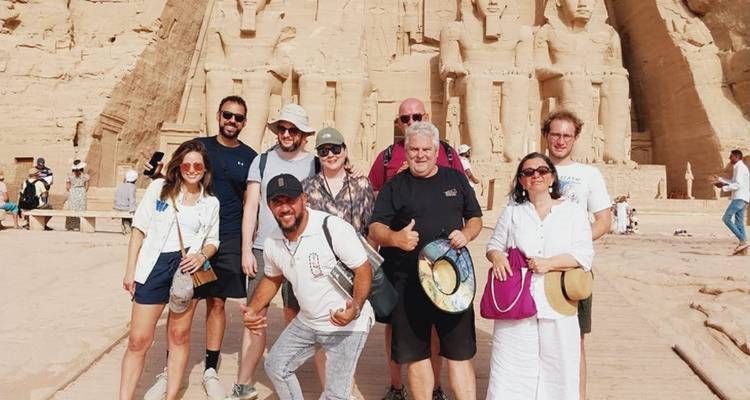 Gran grupo de turistas posando frente a las estatuas colosales de Abu Simbel bajo el brillante sol del desierto.