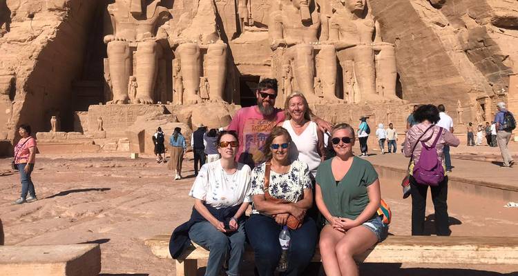 Pequeño grupo de viajeros sentados en un banco frente a las estatuas colosales de Abu Simbel.