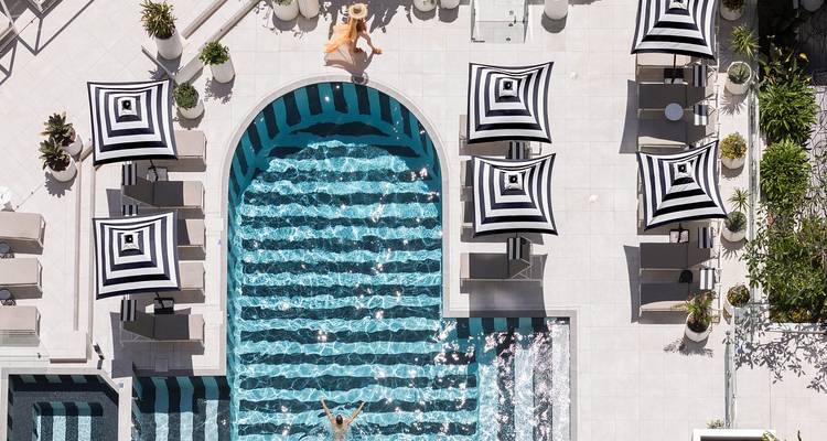 Vue aérienne stylée d'une terrasse de piscine rayée avec nageurs et parasols.