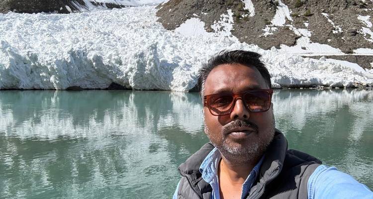 Selfie d'un voyageur à côté d'un lac alpin turquoise avec un énorme glissement de neige derrière.