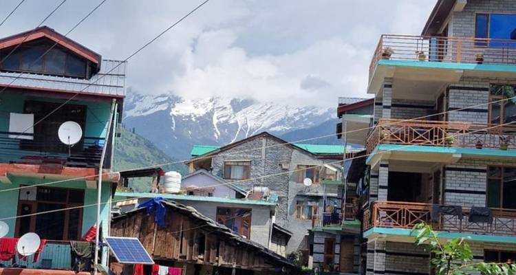 Rue de ville de montagne avec des bâtiments aux paraboles satellitaires et des pics enneigés de l'Himalaya visibles derrière les nuages.