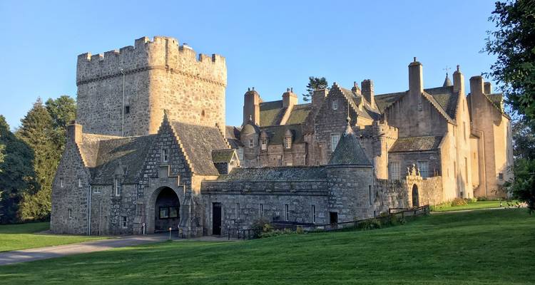 Château de pierre avec tour centrale et portail voûté situé dans des pelouses soignées