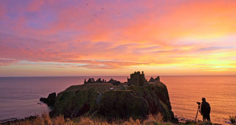 Lever de soleil vibrant sur les ruines d'un château côtier avec photographe en silhouette