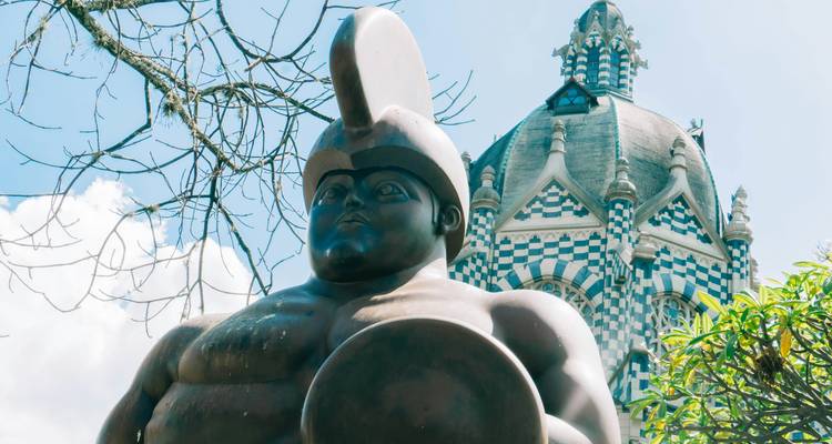 Escultura masiva de bronce de Botero frente a un palacio cultural de tablero de ajedrez bajo cielos brillantes