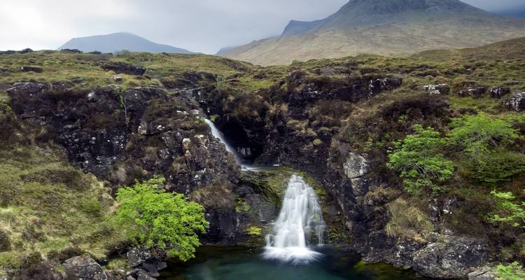 Waterfall in a lush green landscape with mountains in the background.