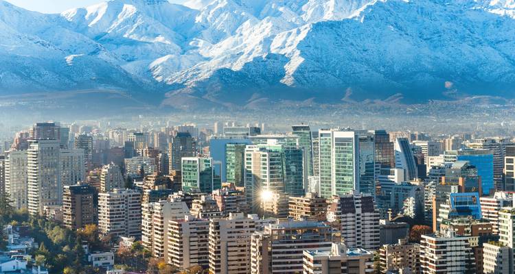 Skyline-Blick auf eine moderne Stadt mit schneebedeckten Bergen im Hintergrund.