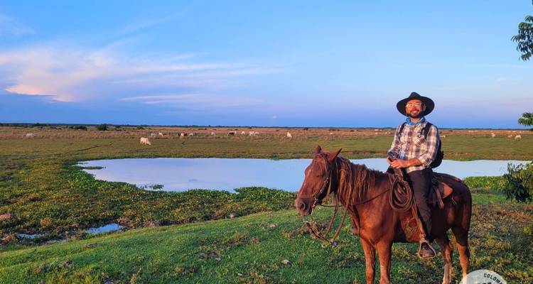 Llanero cowboy on horseback beside a reflective pond at dusk in the Colombian plains.