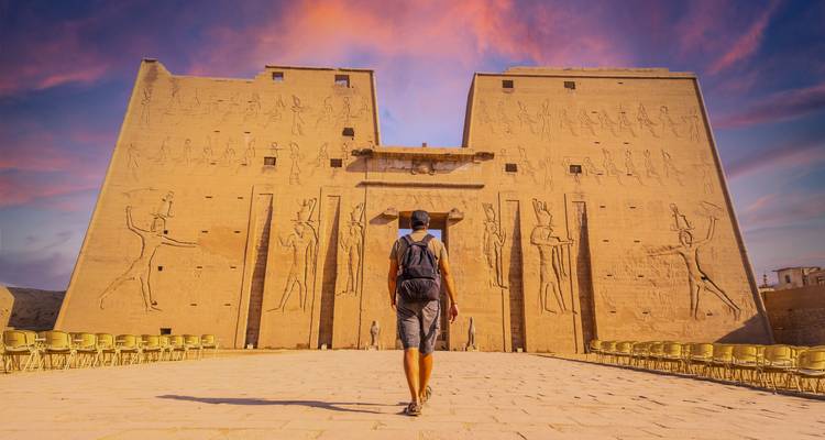 Une personne marchant vers un grand temple ancien sous un ciel coloré.