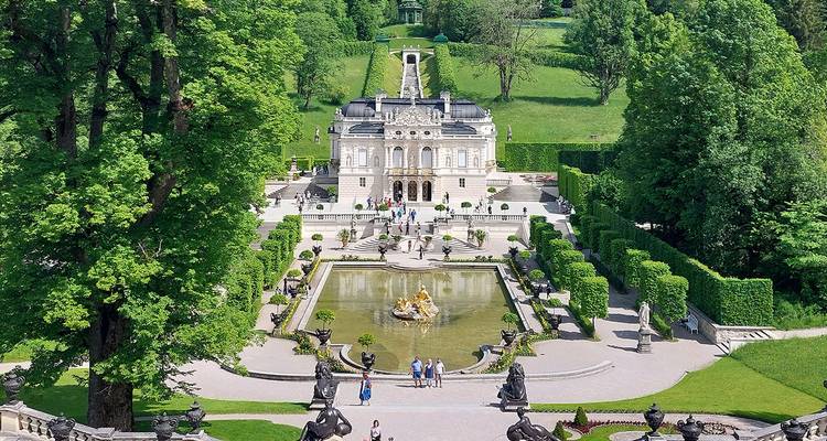 Ornate Linderhof Palace with terraced gardens, fountain pool, and lush forested hills in Bavaria.