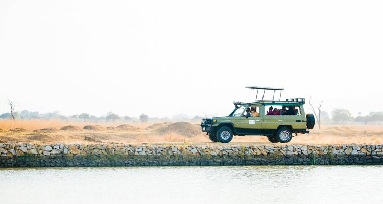 Safari vehicle driving through a dry landscape near a water body.
