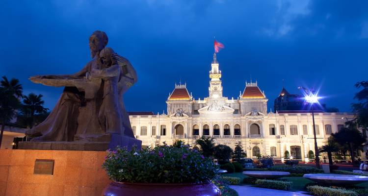 Standbeeld en verlicht gebouw bij zonsondergang op een stadsplein.