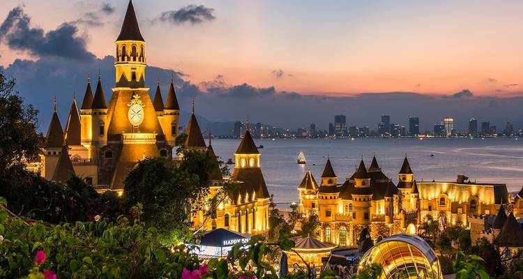 Een fantasie-themapark met een kasteel en stadshorizon bij schemering.