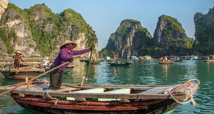 Des habitants locaux pagayant en bateau dans la baie d'Halong parmi les karsts calcaires.