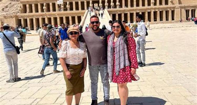 Three people in front of an ancient temple complex with others in the background.